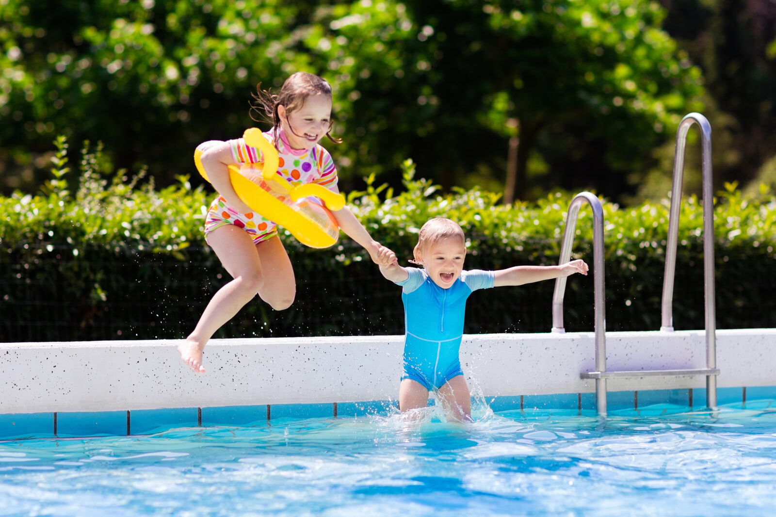 An excited young boy and girl jump into an outdoor pool holding hands. One is wearing a yellow float around her waist. The image is the main image for an LCA blog post on Water Safety Month.