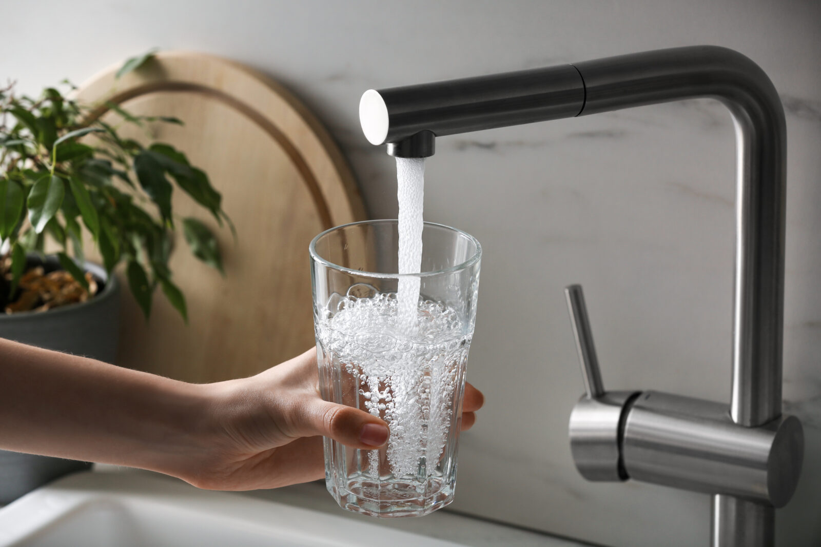 A woman fills a glass with tap water. August is national Water Quality Month.